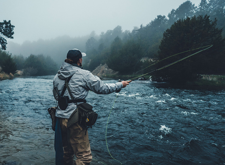 Ein Angler steht im Nebel an einem Fluss