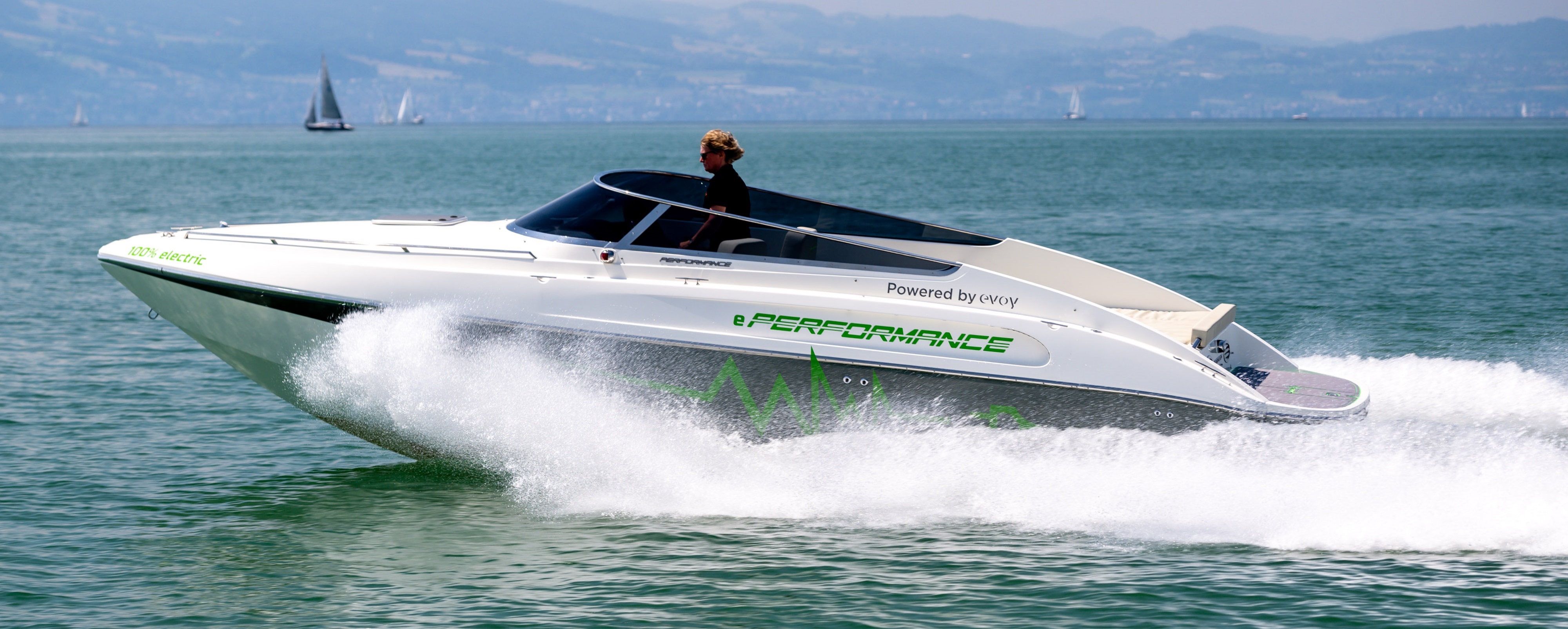 Das Motorboot Performance e801 auf dem Wasser. Im Hintergrund sind mehrere Segelboote und eine Bergkette.