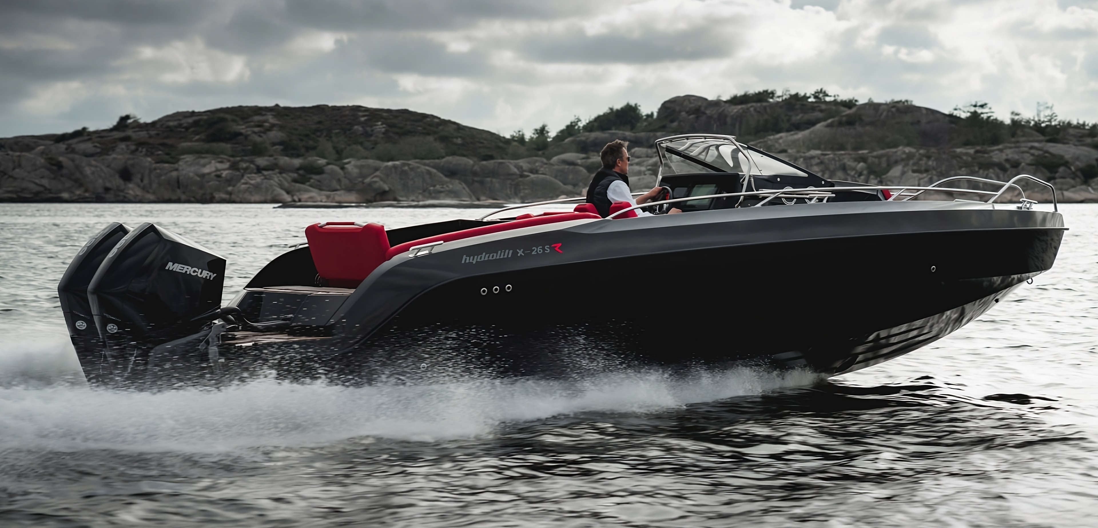 Die schwarze hydrolift X-26S im Wasser. Am Steuer ein Mann. Im Hintergrund ist eine karge, niedrige Bergkette vor einem wolkenverhangenen Himmel.