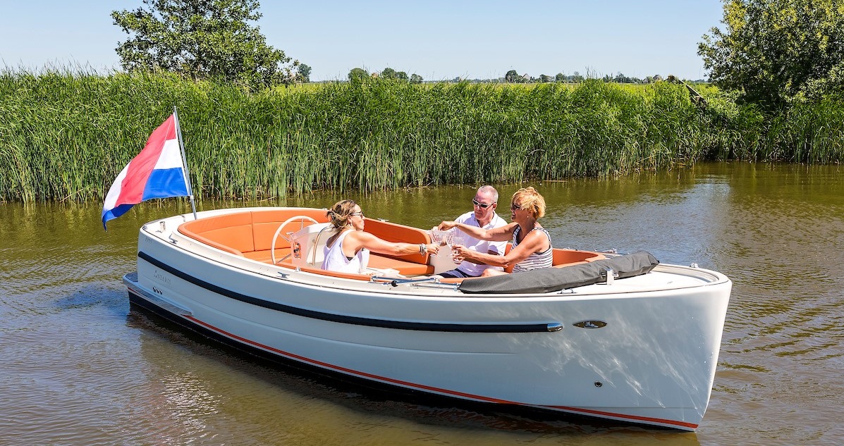Die weiße Antaris fifty5 in einem Binnengewässer. Auf dem Boot sitzen zwei Frauen und ein Mann jeweils mit Sonnebrille, die sich zuprosten. Am Heck weht die niederländische Flagge,
