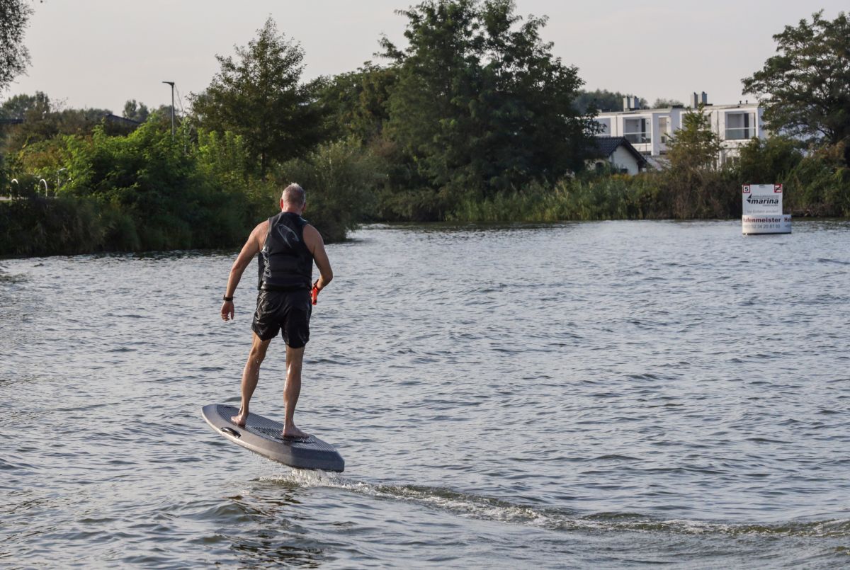 Ein Mann auf einem elektrischen Surfbrett im Wasser, mit dem Ufer im Hintergrund. Ein Mann auf einem elektrischen Surfbrett im Wasser, mit dem Ufer im Hintergrund.