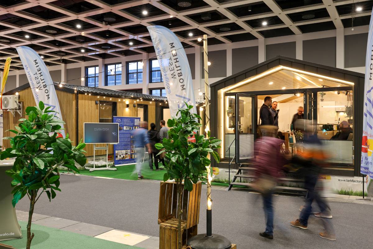 Tiny Houses auf einer Ausstellungsfläche in einer Messehalle sowie vorbeigehende Besucher.