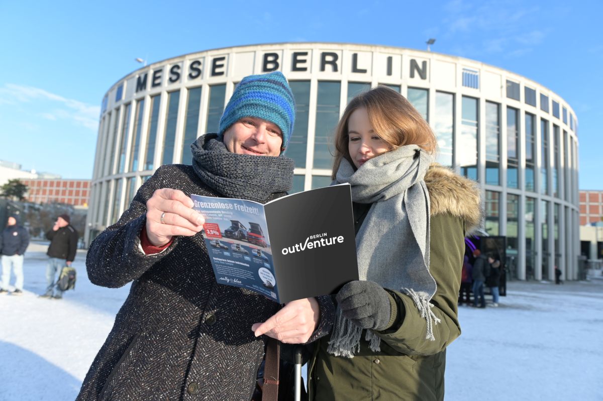 Zwei Personen, die in eine Broschüre über die OutVenture schauen und vor dem Südeingang der Messe Berlin stehen.