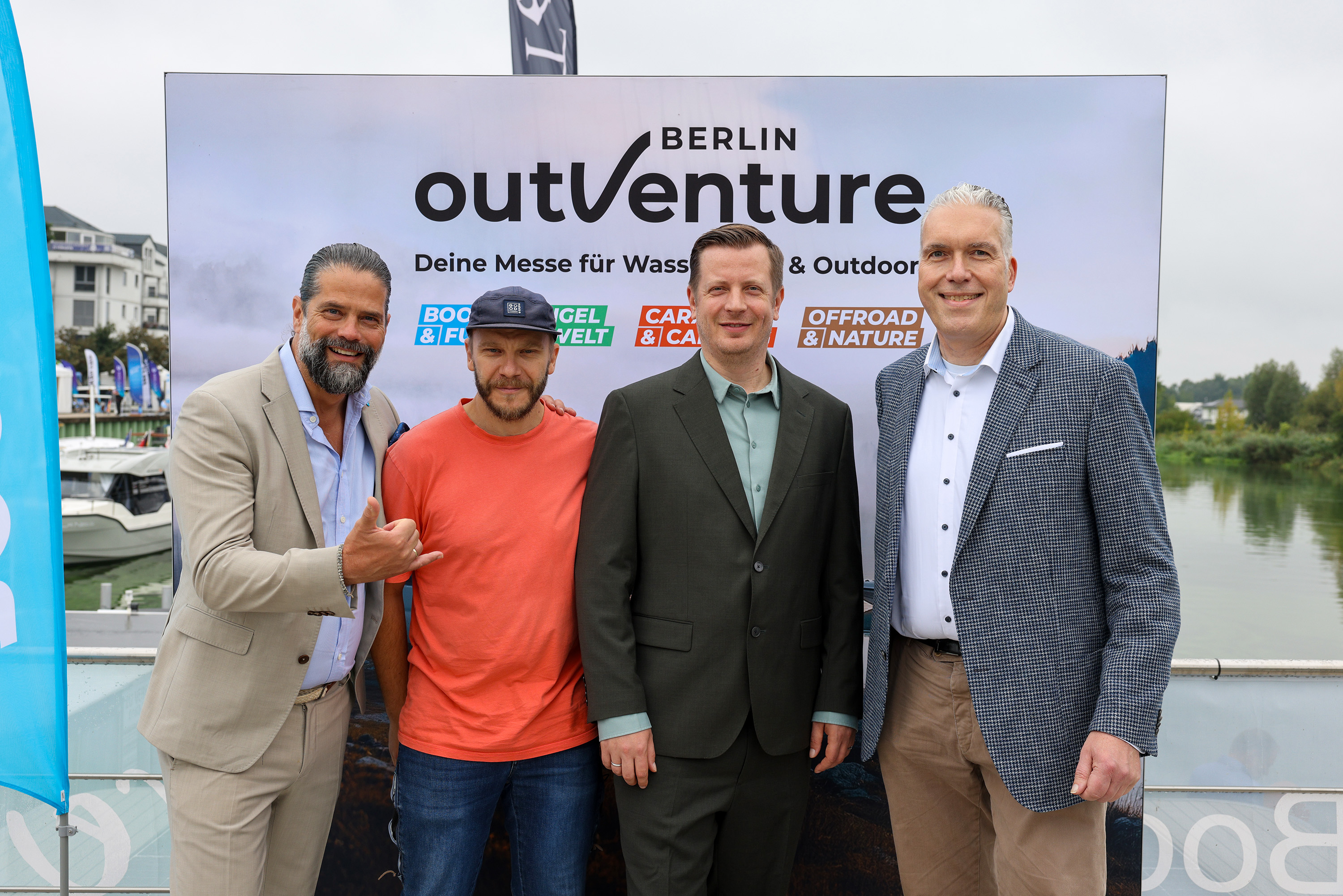 Vier lächelnde Personen vor einer Pressewand mit dem Logo ‚OutVenture Berlin‘ Vier lächelnde Personen vor einer Pressewand mit dem Logo ‚OutVenture Berlin‘